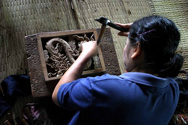 Someone carving an intricate design into a block of wood, using hammer and chisel.