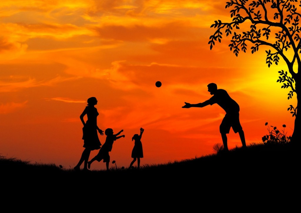 A photo of a family of two adults and two children at sunset - they are all in silhouette against the sky