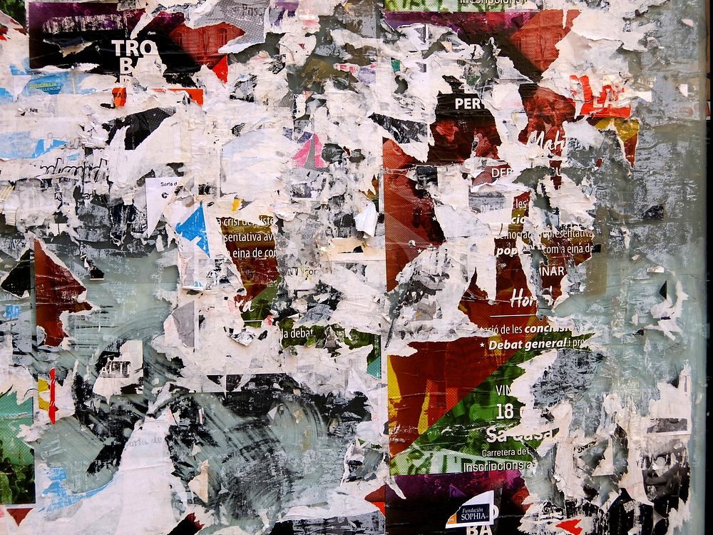 A wall with posters stuck to it. Some posters have been partly ripped off to reveal older posters that were already there.